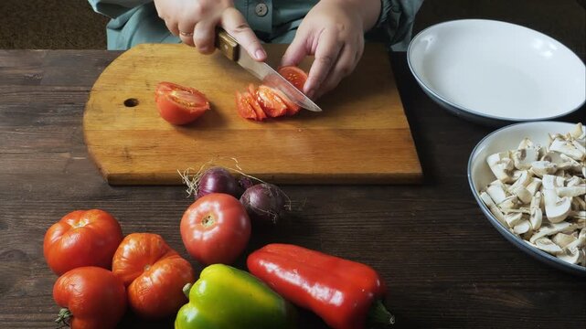 A woman's hands cut fresh red tomatoes with a knife on a cutting board