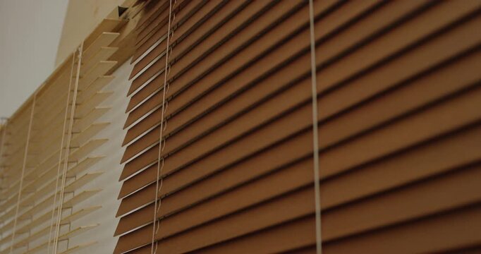 Low angle view of brown wooden venetian blind with horizontal slats and white pull cords in sunlight