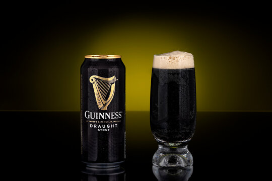 Guinness Draught stout beer can beside filled glass with foam head photographed on dark background. Irish stout beer brand packaging shown as illustrative editorial.