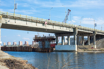 Obraz premium Bridge construction, workers building bridge with large red concrete pumping crane and cement pouring process, infrastructure development in modern transportation project, bridge reconstruction