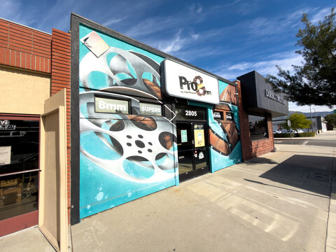 LOS ANGELES, CA, FEB 9, 2026: Wide-angle view of Pro8mm film lab in Burbank, with bold teal film reel mural, clear blue sky, and neighboring Direct Motors