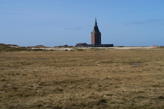 Von der Waggonplattform des Zuges vom Hafen zum Dorf auf der deutschen Nordseeinsel Wangerooge ist der Westturm als Wahrzeichen hinter Salzwiesen zu sehen. Es ist ein sonniger Fr&uuml;hlingstag.