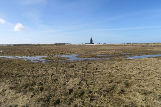 Hinter einem Priel und Salzwiesen ist auf der deutschen Nordseeinsel Wangerooge der Westturm zu erkennen. Gesehen von einer Wagenplattform der Inselbahn auf der Fahrt vom Hafen zum Dorf. 