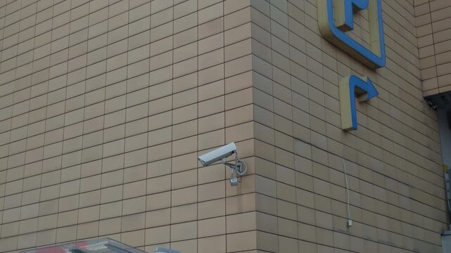 Single security camera overlooking parking area, mounted on beige tiled corner, minimal composition highlights lens and bracket, crisp daylight detail suitable for surveillance and infrastructure