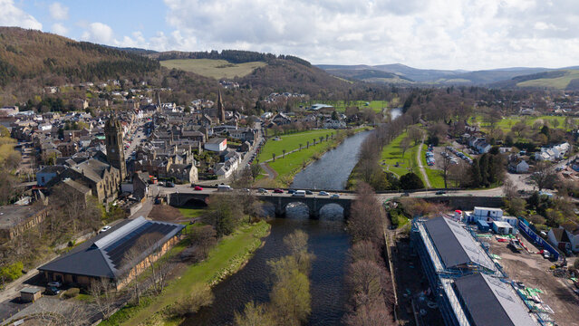 A scenic view of the River Tweed flowing through the Scottish Borders with the historic town of Peebles situated on the left bank. The image captures the calm blue water of the river, lush green trees