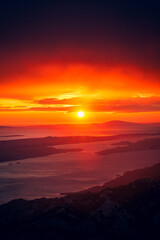 Obraz premium Sun setting over ocean with mountainous coastline