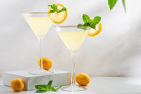 Bright and refreshing cocktail with two glasses of limoncello spritz, garnished with fresh lemon slices and mint sprigs on a white surface, with green foliage in the background