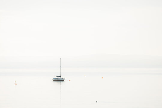 A lone sailboat in a minimalist seascape scene moored on the Firth of Forth in the fog, Aberdour, Fife, UK.