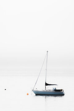 A lone sailboat in a minimalist seascape scene moored on the Firth of Forth in the fog, Aberdour, Fife, UK.