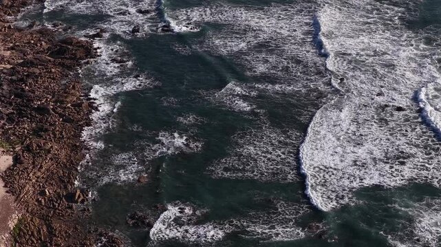 Aerial view of powerful ocean waves crashing against a rugged, rocky coastline, creating a stunning display of nature's force, Vila Praia de Ancora, Portugal.