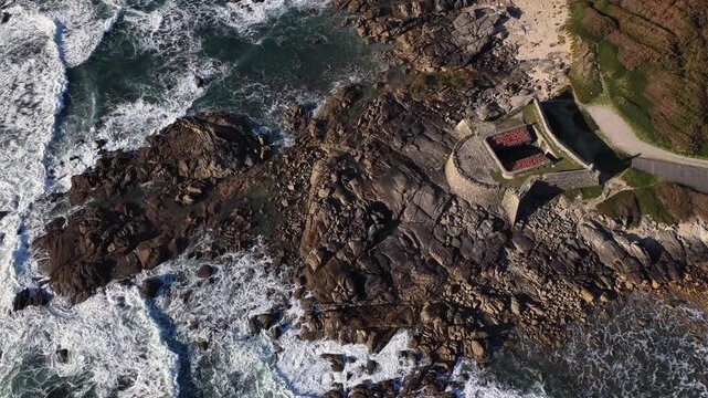 Aerial view of Forte do Cao where the dark, jagged rocks meet the wild, churning sea, creating a dramatic contrast against the fort, Vila Praia de Ancora, Portugal.