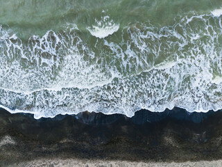 Fototapeta premium Waves crash on the shore at a beach during the day near the ocean