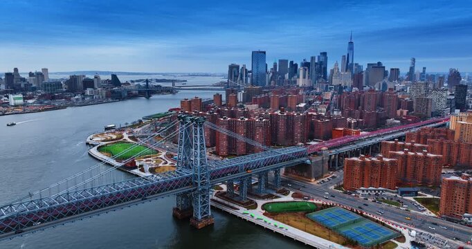 Approaching the support of Williamsburg Bridge with numerous cars riding to and from it. Famous Manhattan skyline in the backdrop.
