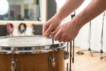 Fototapeta premium Musician using a metal drum key to tune the tension rods of a wooden snare drum in a recording studio
