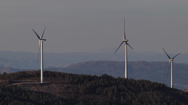 Aerial view of stark white wind turbines standing tall against a backdrop of rolling hills and a pale sky, a testament to renewable energy, Amarante, Portugal.