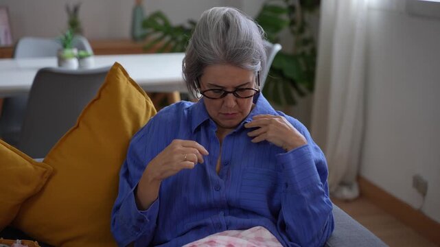 Senior woman sewing a button on her shirt at home