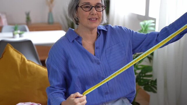 Mature woman dressmaker measuring fabric with tape