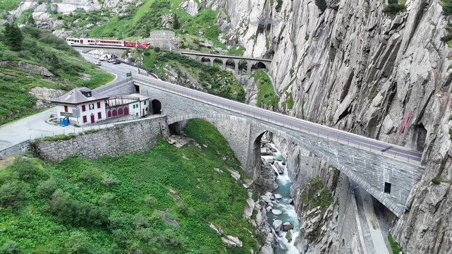 Panorama flight over second and third Teufelsbr&uuml;cke (Devil's Bridge) and Sch&ouml;llenenbahn railway bridge with train over Sch&ouml;llenen Gorge in the Swiss canton of Uri, Switzerland