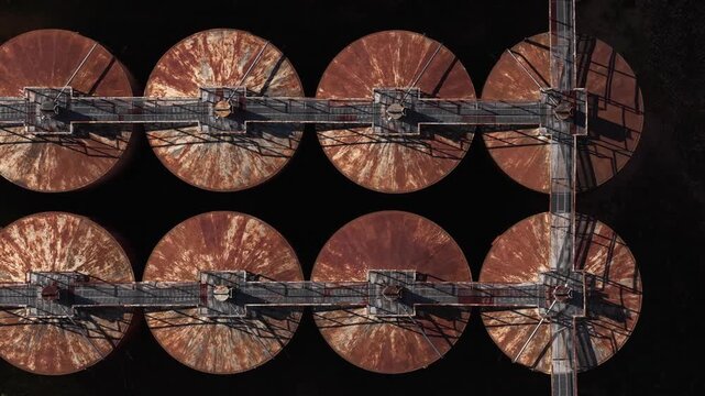 Aerial view of a series of eight rusty, circular silos interconnected by walkways creating a stark contrast against the dark background, Vila Real, Portugal.