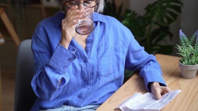 Mature woman drinking water while reading medication instructions