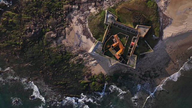 Aerial view of Forte de Insua where the imposing fort stands at the edge of the beach, contrasting with the ocean's waves, Moledo, Portugal.