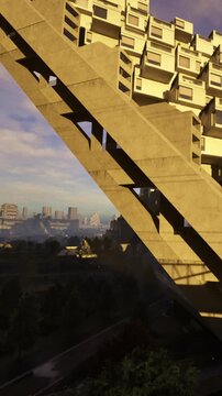 A tall concrete structure displays unique design overlooking a city below. Sunlight shines on the building, highlighting its shapes and forms. The skyline is visible in the distance.