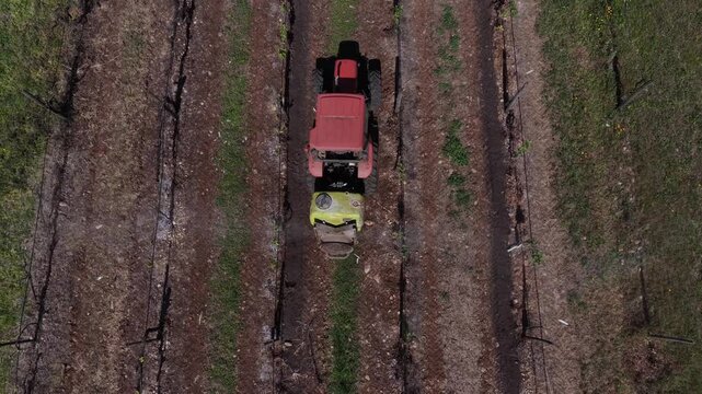 Aerial view of a red tractor with a yellow attachment moving through rows of vines, creating contrasting lines and textures, Viana do Castelo, Portugal.