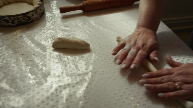 Caucasian woman rolls dough with hands on a floured countertop, using a rolling pin and preparing for baking in a well-lit kitchen environment
