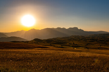 Fototapeta premium Golden hour sun setting over mountain landscape and grassy field