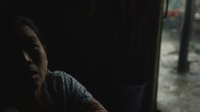 Portrait of a middle aged asian woman resting in her dark shack in an unregulated oil field