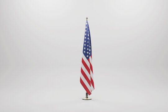high-quality, professional studio shot of the United States flag hanging vertically on a gold-finished indoor flagpole. Isolated on a clean, neutral light gray background with soft shadows.