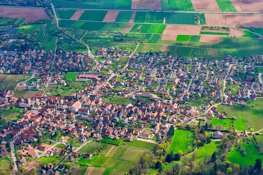 Aerial view of the charming village nestled amid patchwork fields and vineyards, a tapestry of earth tones contrasted by vibrant greens, Kintzheim, Grand Est, France.