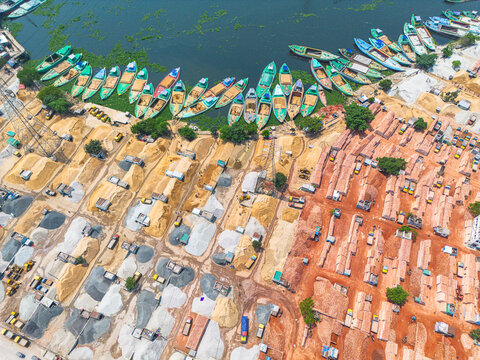 Aerial view of boats docked along the murky river's edge beside piles of sand and brick in contrasting earthy tones, Dhaka, Dhaka Division, Bangladesh.