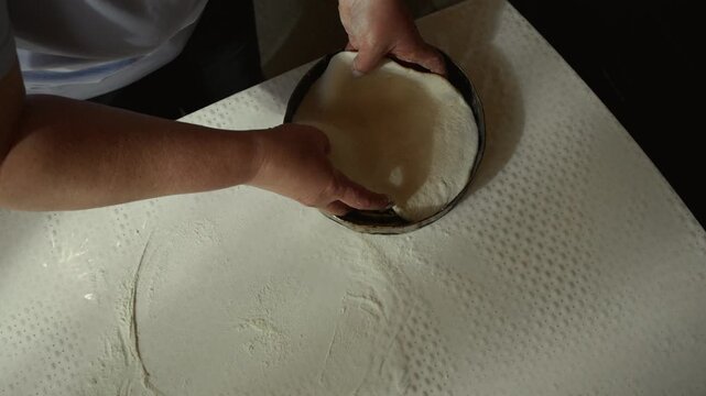 Female baker prepares dough by shaping and pressing it into a round form inside a well-lit kitchen with a clean countertop and baking tools visible