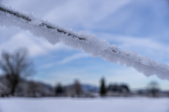 View of crystalline frost clinging to a wire against a backdrop of a blurred winter landscape under a pale sky, Schwangau, Bavaria, Germany.