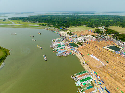 Aerial view of boats lined up along the riverbank, reflecting the sky, next to a vast, flat land filled with rows of what appear to be haystacks, Charmonai, Bangladesh.