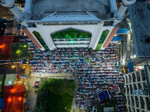 Aerial view of rows of people praying beneath the grand mosque, with its white minarets reaching towards the sky, Charmonai, Barisal Division, Bangladesh.