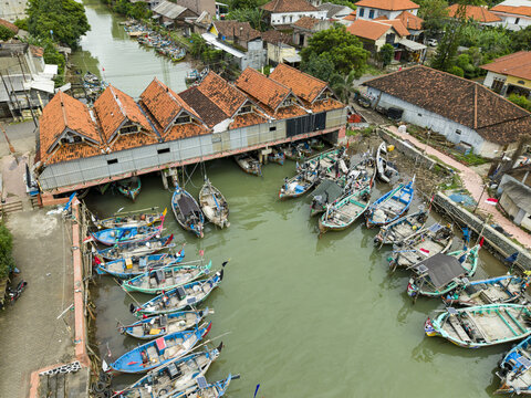 Aerial view of fishing boats clustered at the Jepara Floating Fish Market, a vibrant scene where rustic vessels meet the earthy tones of tiled roofs, Jepara, Central Java, Indonesia.