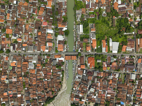 Aerial view of a river cutting through a dense urban landscape with vibrant red-tiled roofs contrasting against the green river and trees, Jepara, Central Java, Indonesia.