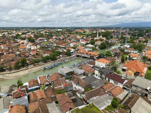 Aerial view of the Jepara Floating Fish Market, where boats cluster, reflecting the sky amid the town's terracotta roofs, Jepara, Central Java, Indonesia.