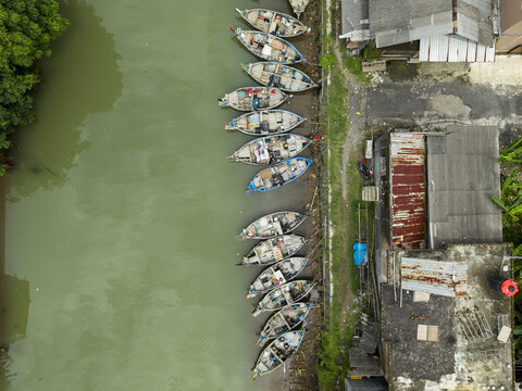 Aerial view of fishing boats resting along the riverbank, creating a mosaic of colors and textures next to waterside buildings, Jepara, Central Java, Indonesia.