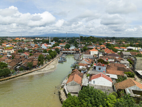 Aerial view of a vibrant town where the river meets the sea, its terracotta rooftops contrasting with the lush greenery, Jepara, Central Java, Indonesia.