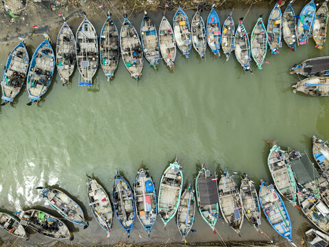 Aerial view of numerous boats, tightly packed along the Jepara Floating Fish Market's edge, create a textured mosaic on the water, Jepara, Central Java, Indonesia.