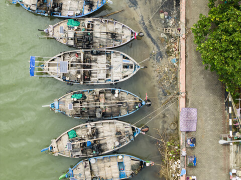 Aerial view of fishing boats moored along the coast near Jepara Floating Fish Market, with vibrant turquoise accents contrasting with the weathered wood, Jepara, Central Java, Indonesia.