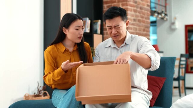 A man and a woman are sitting on a couch in a modern living room. They are unboxing a package together. The setting features brick walls and contemporary decor.