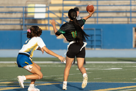 Female flag football quarterback preparing to throw pass while defender reaches to pull flag during game