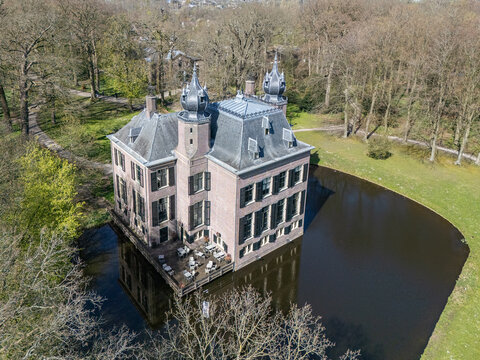 Aerial view of the historic Oud Poelgeest Castle, a stately blush-pink manor standing proudly amidst a dark moat, surrounded by bare trees, Oegstgeest, Zuid-Holland, Netherlands.