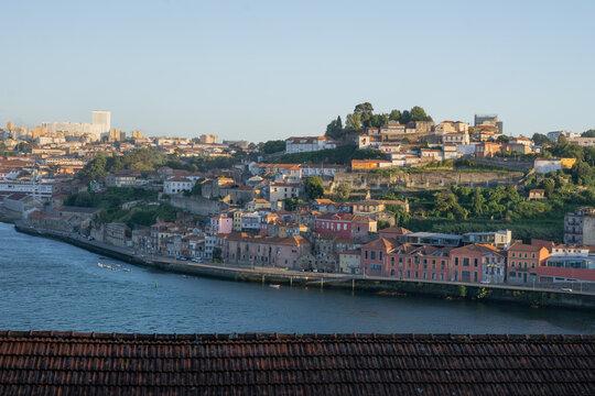 View of terracotta rooftops cascade into the Douro River, where colorful buildings line the waterfront under a soft, golden light, Porto, Porto District, Portugal.