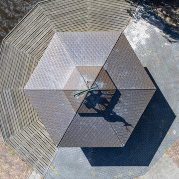 Aerial view of the geometric patterns of a hexagonal structure with brown tiles and a central metal feature, casting shadows on the surface, Tollebeek, Flevoland, Netherlands.