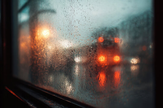 Moody rainy street scene seen through wet window. Abstract blurry impressionistic view. Shallow depth of field.